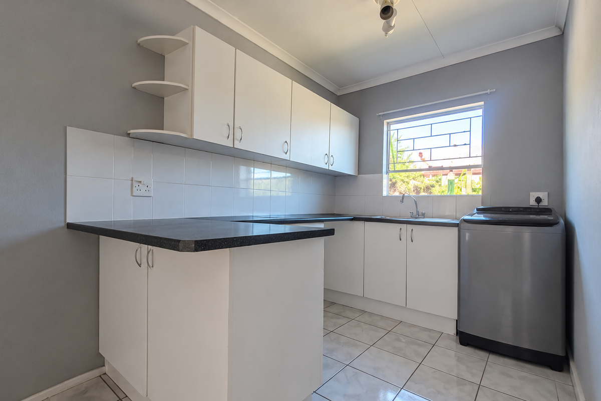 A functional kitchen featuring white built-in cabinetry, dark laminate countertops, tiled splashbacks, and a window with security bars.