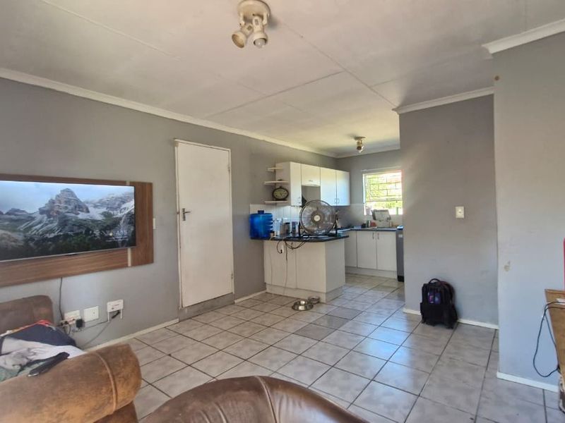 Open-plan living and kitchen area featuring tiled flooring, functional cabinetry, and natural light through a window with security bars.