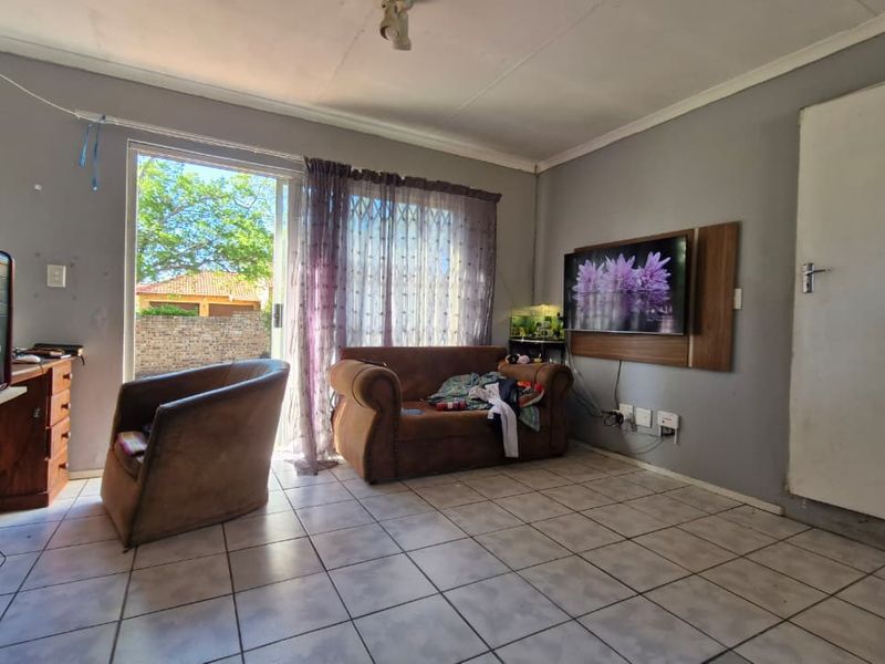 A living room featuring tiled flooring, a sliding glass door providing outdoor access, and a wall-mounted TV panel.