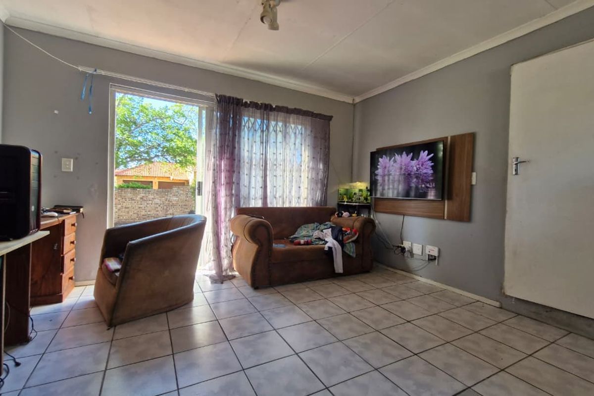 A living room featuring tiled flooring, a sliding glass door providing outdoor access, and a wall-mounted TV panel.