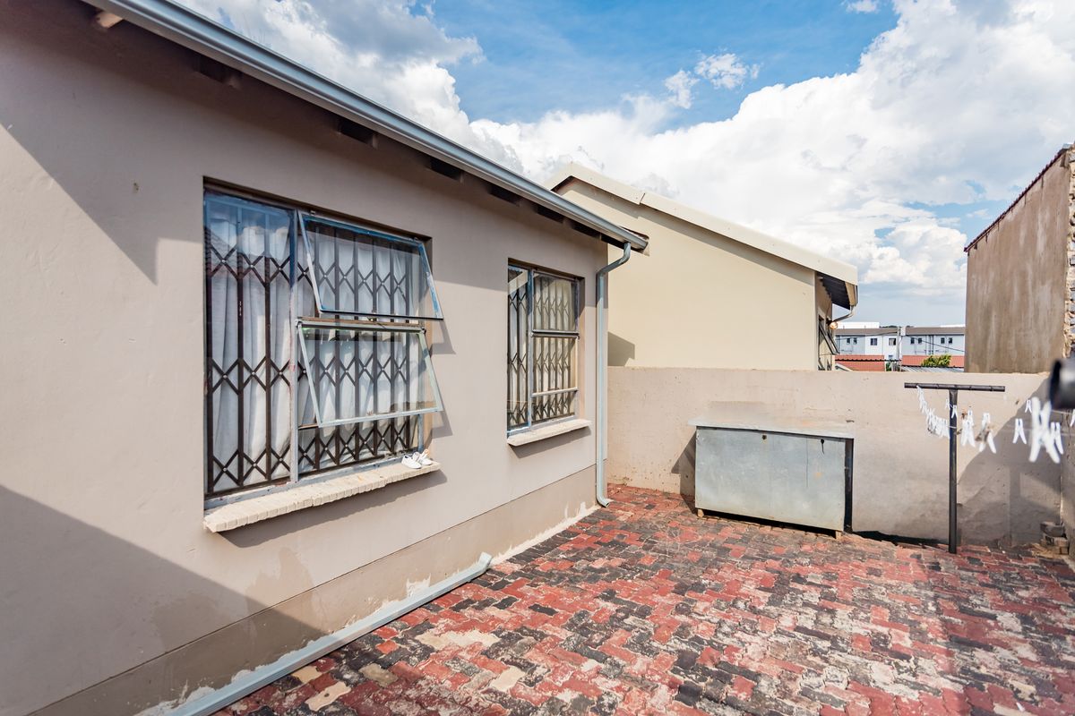 Rear exterior view of the property featuring a paved patio area, security gates on windows, and a boundary wall.