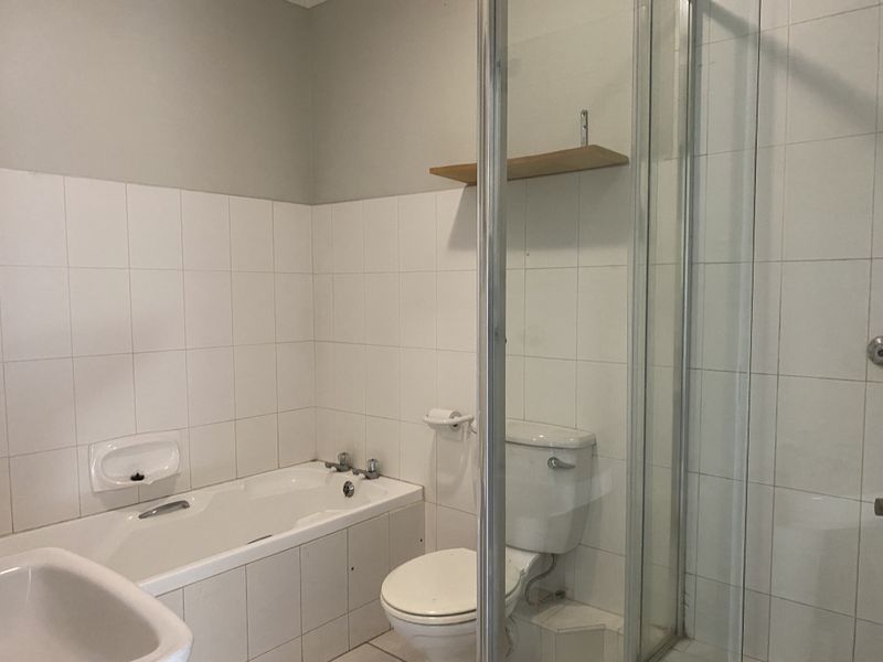 A functional bathroom featuring a built-in bathtub, separate shower enclosure, and toilet with neutral wall tiling.