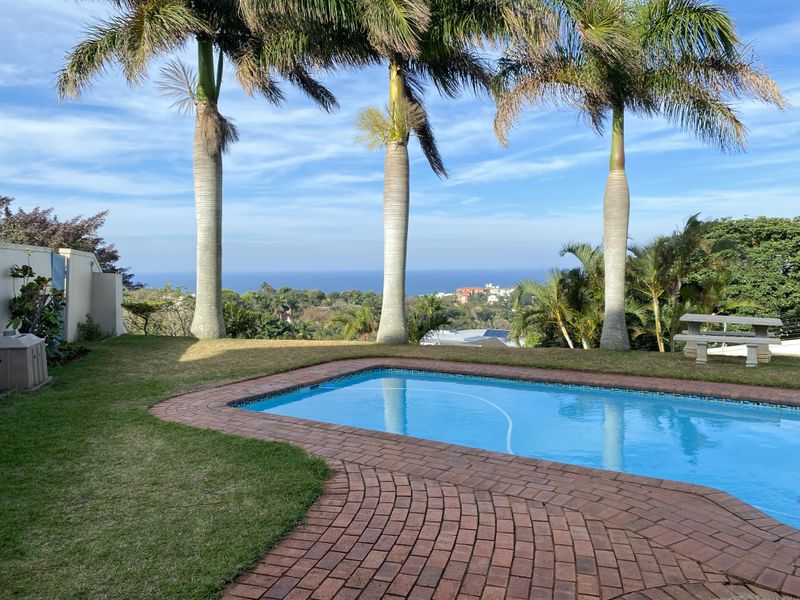 Outdoor pool area featuring brick paving, established palm trees, and expansive coastal views.