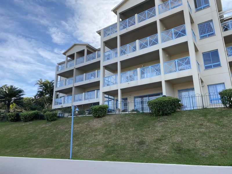 Rear elevation of a multi-story apartment building featuring stacked balconies with blue metal railings, sliding glass doors, and a well-maintained lawn area.