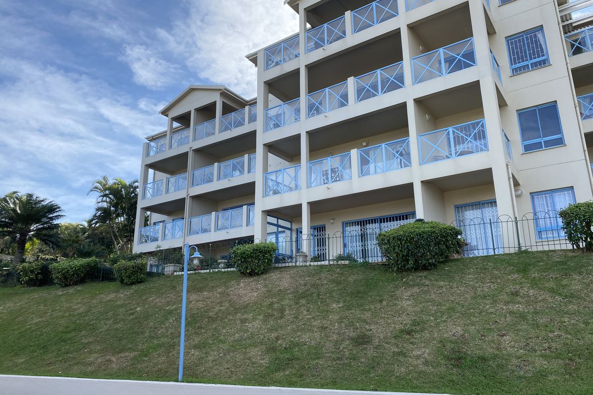 Rear elevation of a multi-story apartment building featuring stacked balconies with blue metal railings, sliding glass doors, and a well-maintained lawn area.