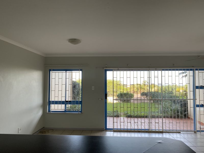 An empty open-plan living area featuring tiled floors, large sliding glass doors with security gates, and direct access to an outdoor patio area.