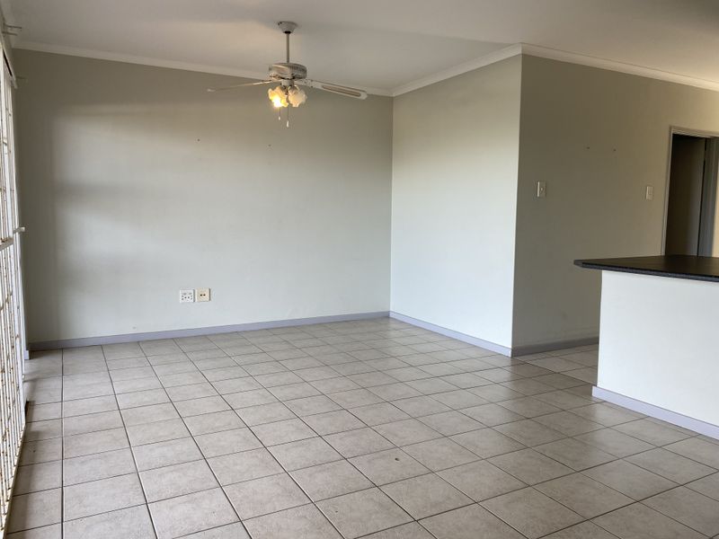 Spacious open-plan living area featuring neutral tiled flooring, a ceiling fan, and a breakfast bar, offering a versatile layout for dining and relaxation.