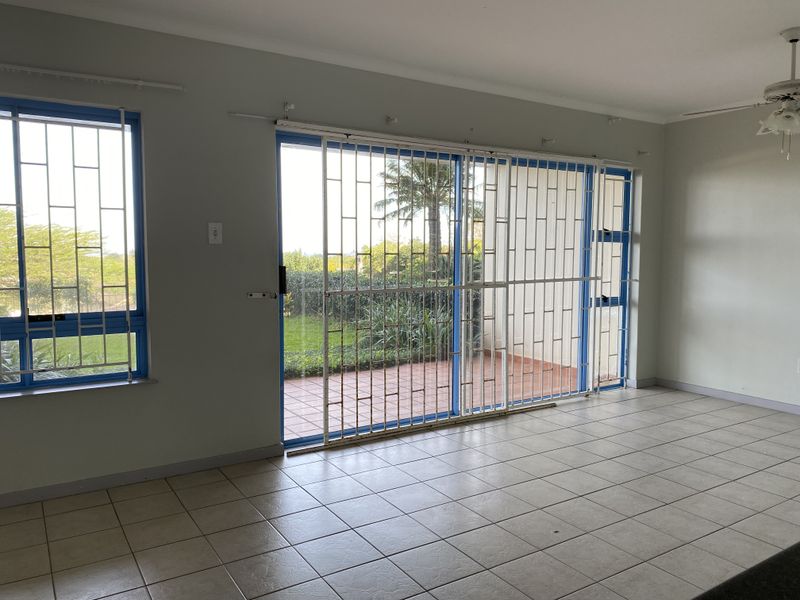 An empty living room featuring tiled flooring, a ceiling fan, and large sliding glass doors with security gates leading to an outdoor patio area.
