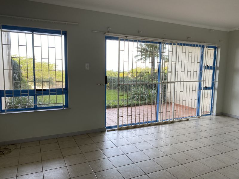 An empty living area featuring tiled flooring, large windows with security bars, and a sliding glass door leading to an outdoor patio space.