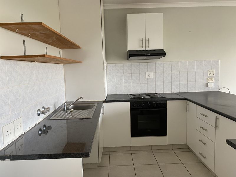 A functional kitchen featuring built-in cabinetry, a black electric hob with oven, extractor fan, and tiled backsplash with ample counter space.