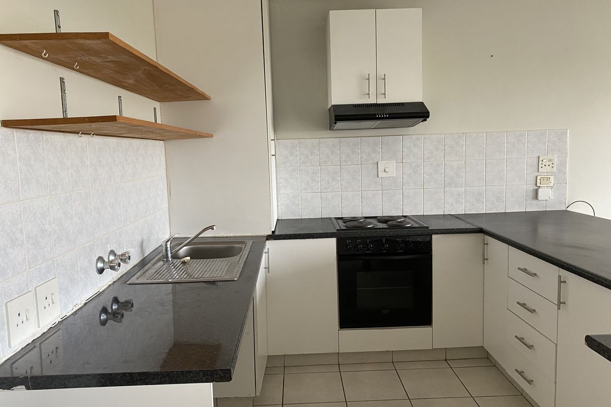 A functional kitchen featuring built-in cabinetry, a black electric hob with oven, extractor fan, and tiled backsplash with ample counter space.