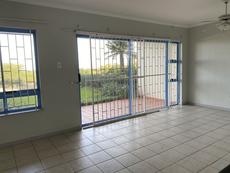 Spacious living area featuring neutral tiled flooring, a ceiling fan, and large sliding glass doors with security gates leading to an outdoor patio.