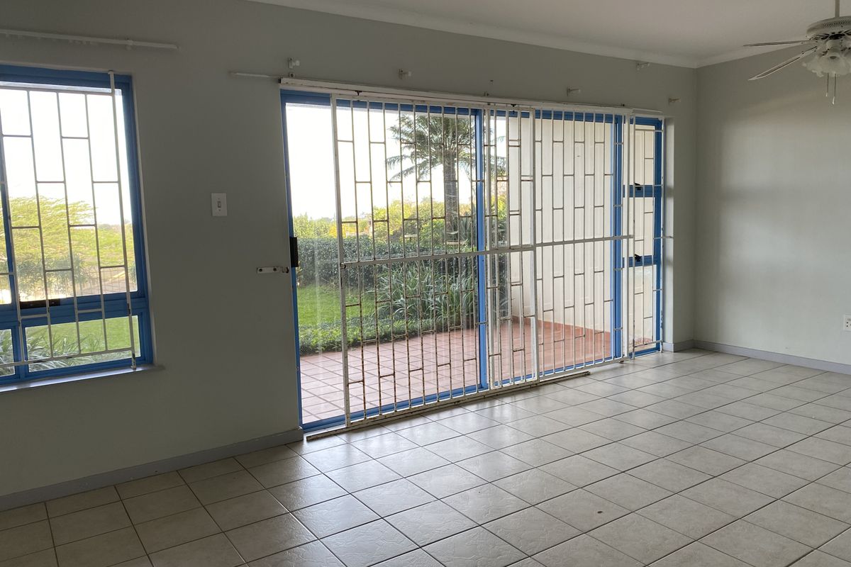 Spacious living area featuring neutral tiled flooring, a ceiling fan, and large sliding glass doors with security gates leading to an outdoor patio.