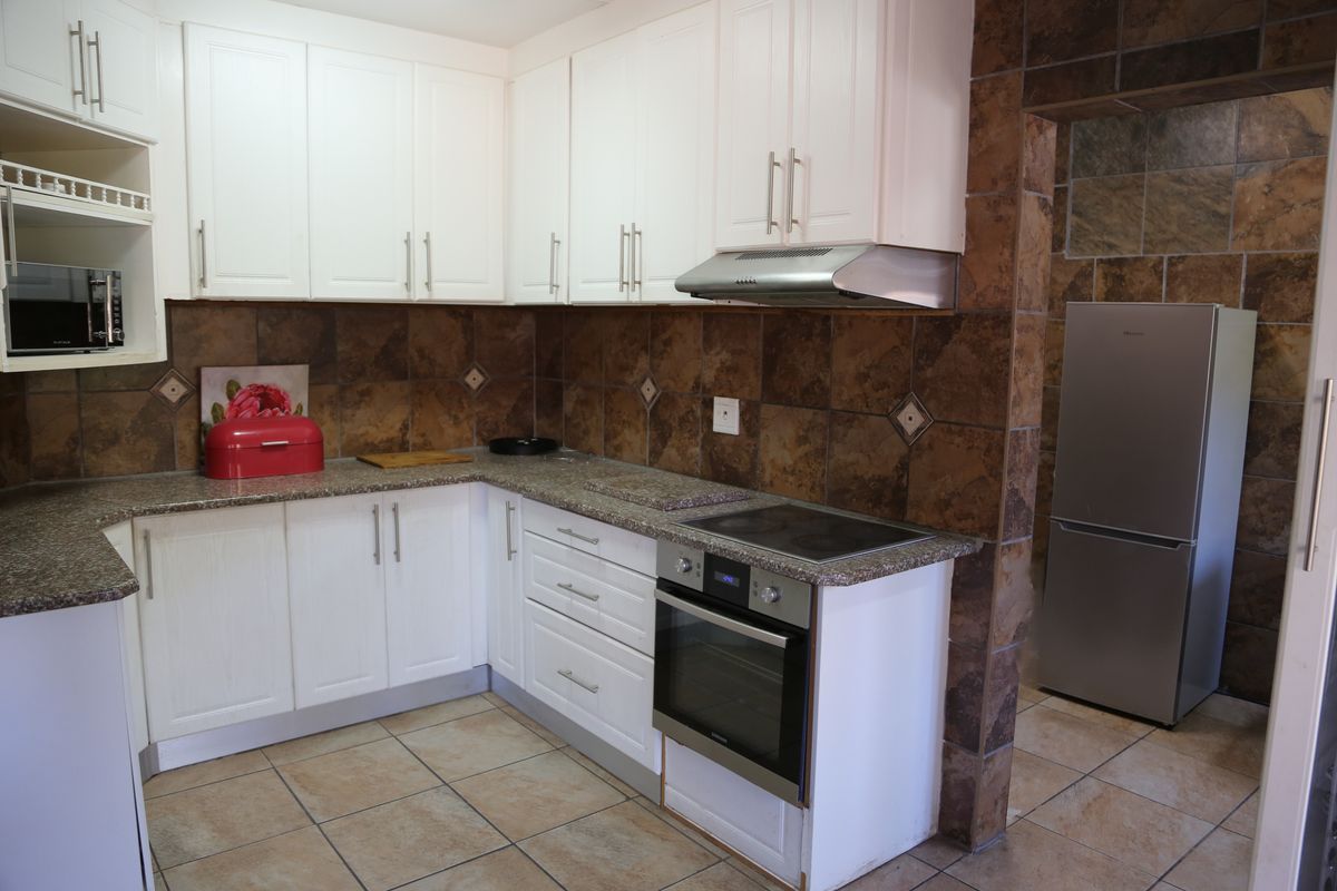A functional kitchen featuring white cabinetry, granite countertops, a built-in oven with electric hob, and tiled splashbacks.