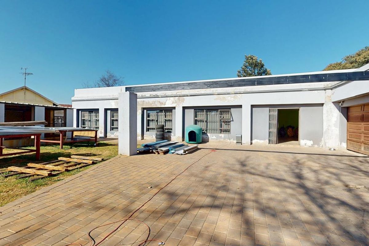 Rear exterior view of the property featuring a paved courtyard, garage access, and multiple windows with security bars, showing signs of exterior wear.