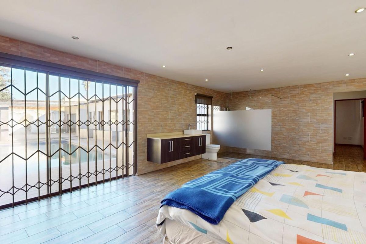 Spacious bedroom featuring stone-look wall cladding, tiled flooring, an integrated floating vanity with vessel sink, and direct access to the pool area.