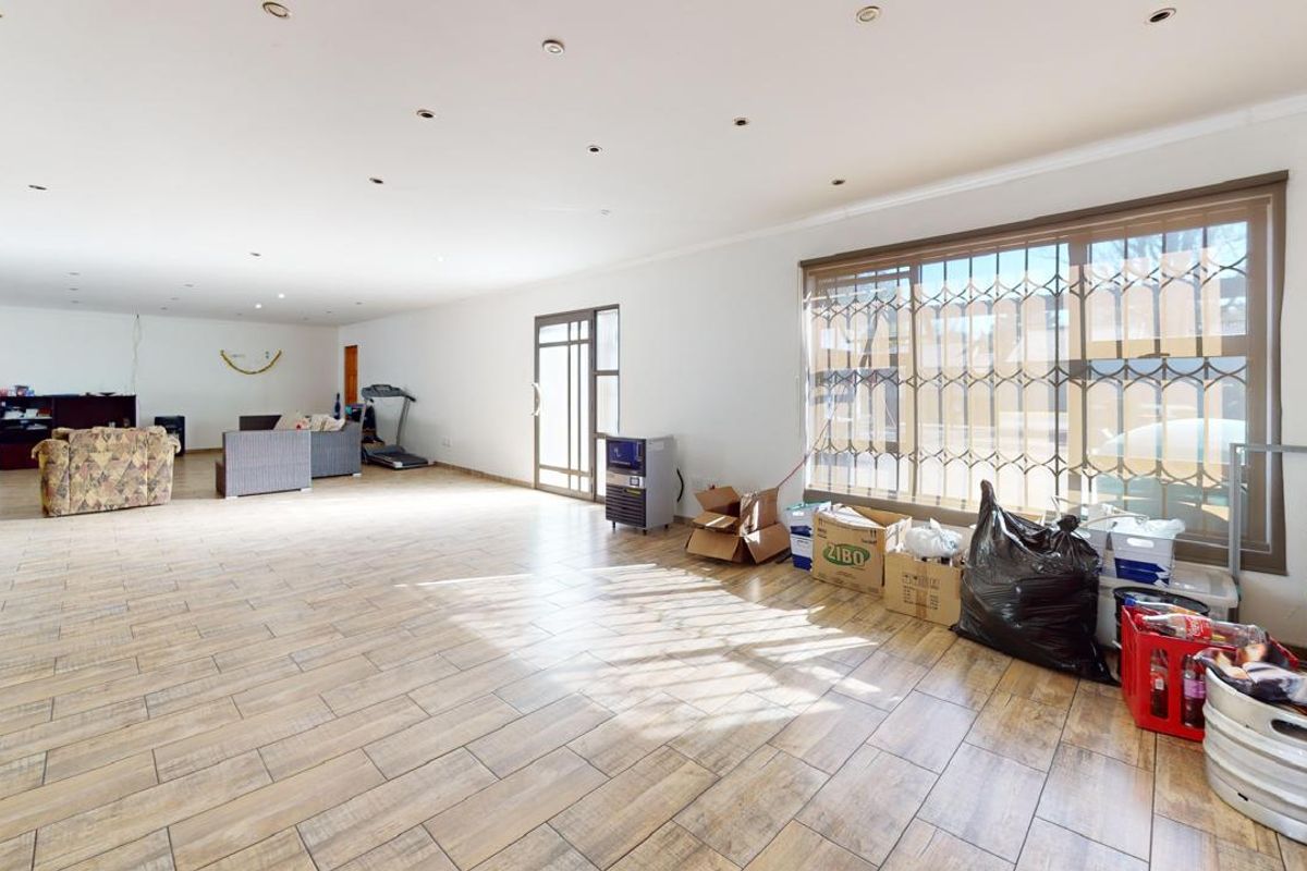 Spacious open-plan living area featuring tiled flooring, recessed downlighting, and large windows with security bars.