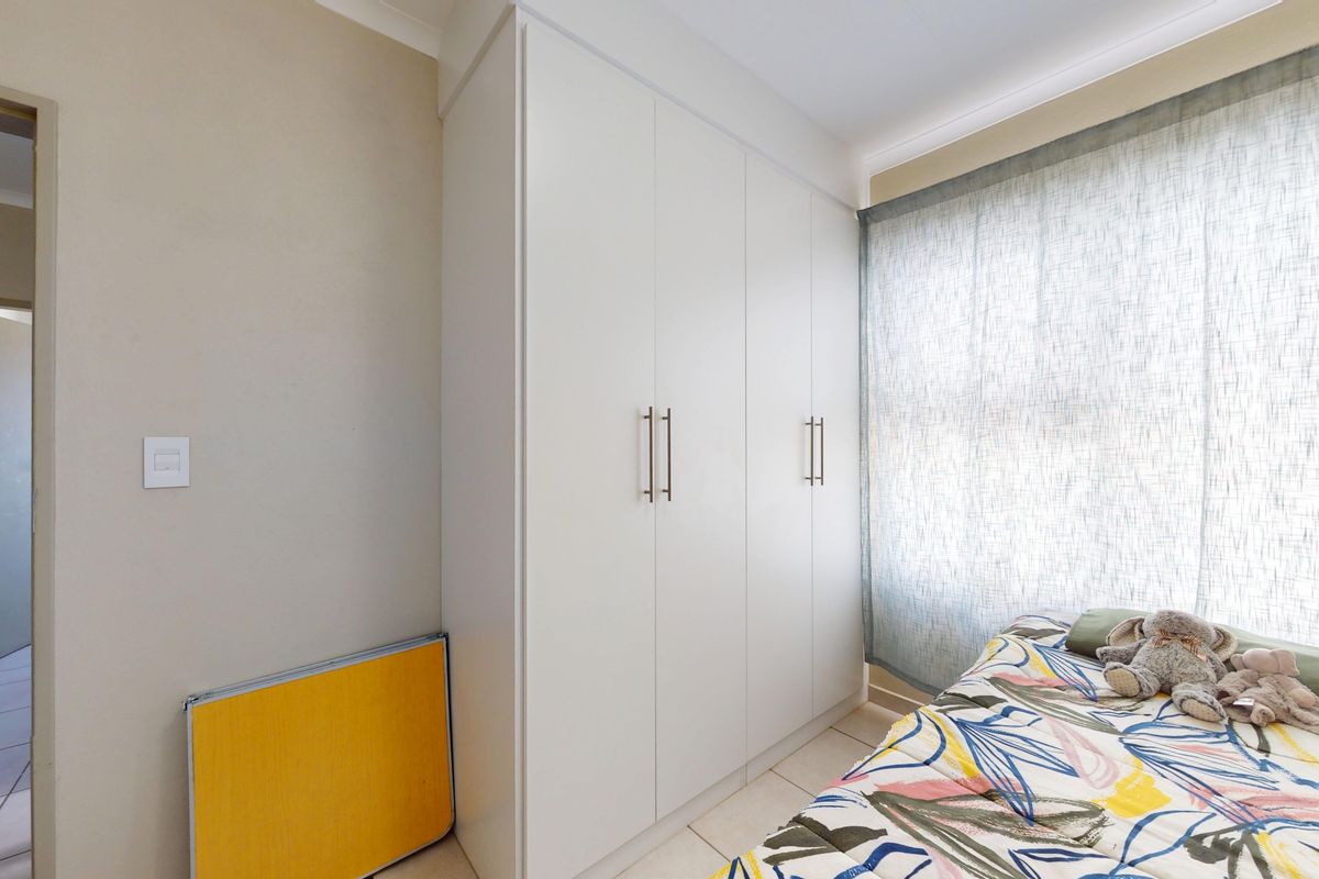 A bedroom featuring neutral walls, tiled flooring, and white built-in cupboards with modern handles.