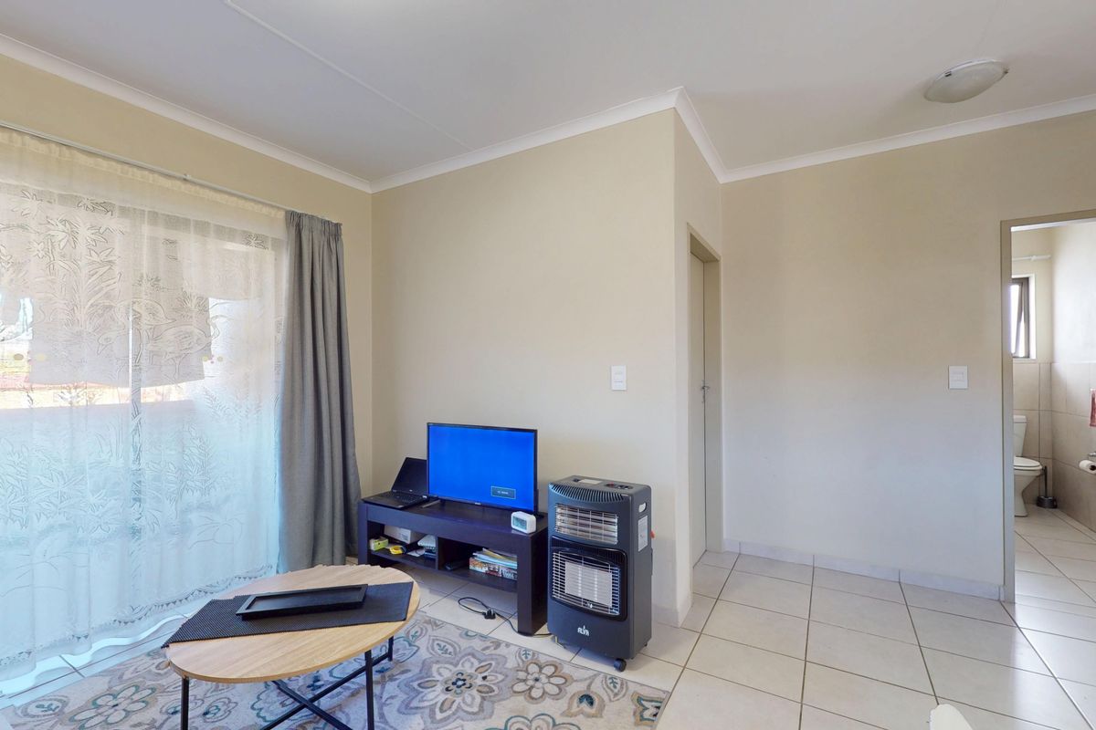 A living room featuring tiled flooring and a sliding glass door providing natural light, with an adjacent doorway leading to a bathroom.