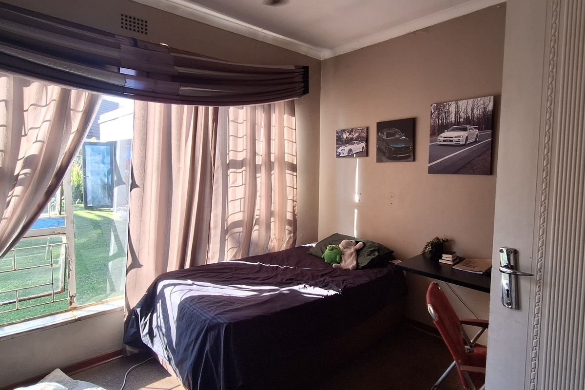 A bedroom featuring a large window with garden views, neutral wall tones, and carpeted flooring.