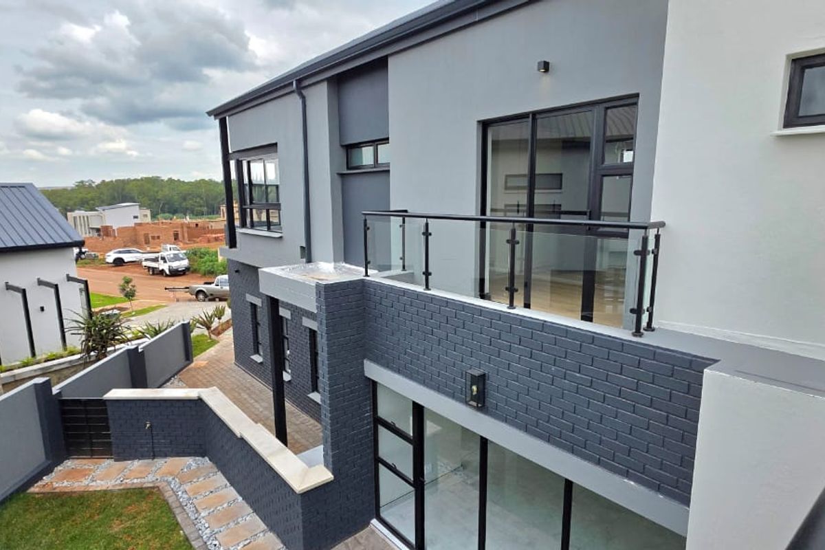 Modern double-story rear elevation featuring a glass balustrade balcony, dark brick accents, and paved garden pathways.