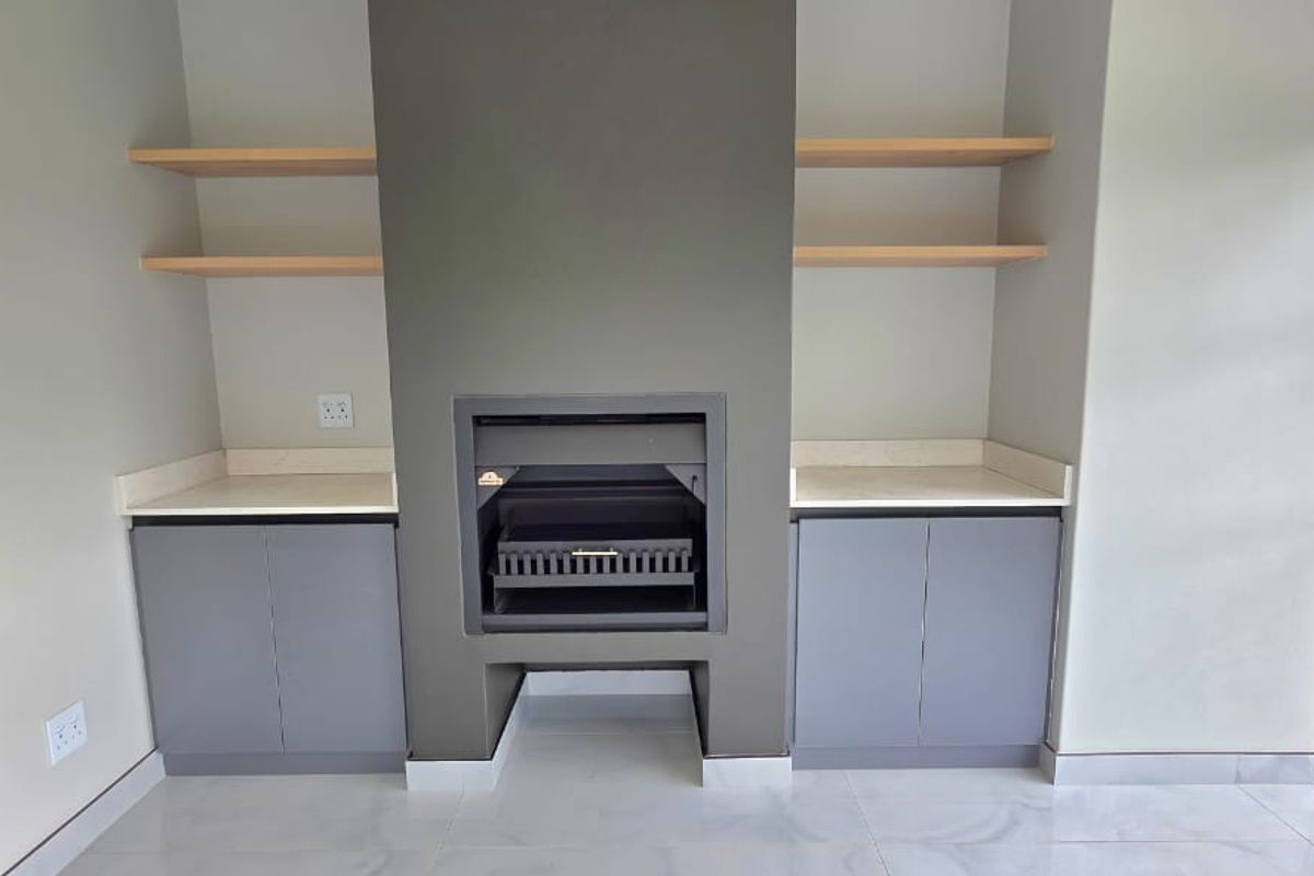 Modern living area featuring a sleek built-in fireplace, custom cabinetry with stone countertops, floating shelves, and large windows overlooking the garden.