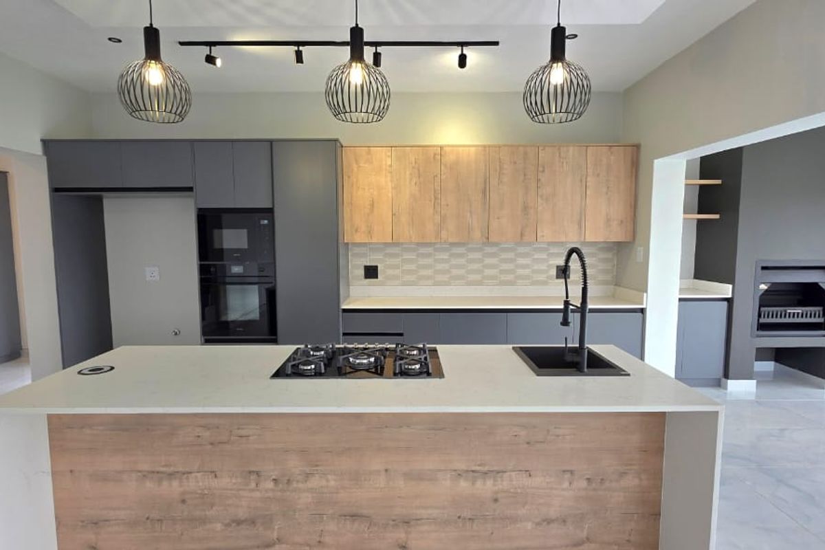 Modern kitchen featuring a central island with gas hob, stone countertops, integrated cabinetry, and a built-in fireplace in the adjacent living area.