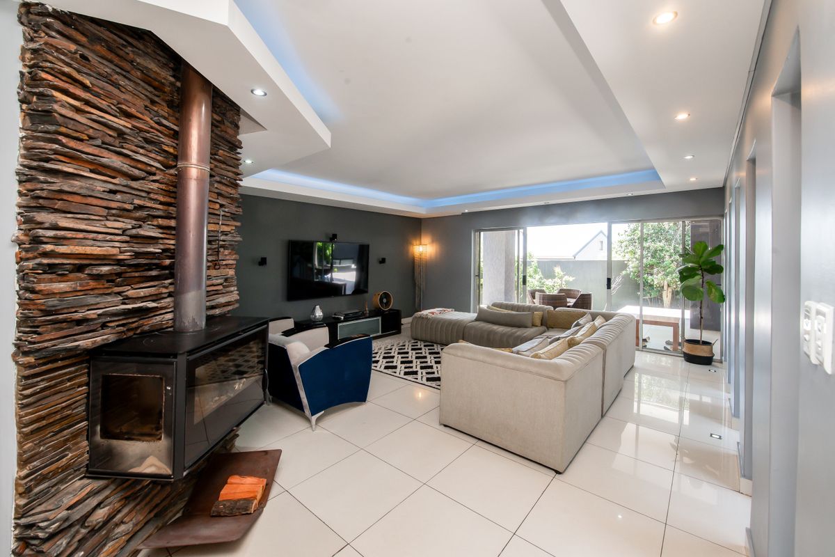 Spacious living room featuring a striking stone-clad fireplace, recessed ceiling lighting, and large sliding glass doors opening to an outdoor patio area.