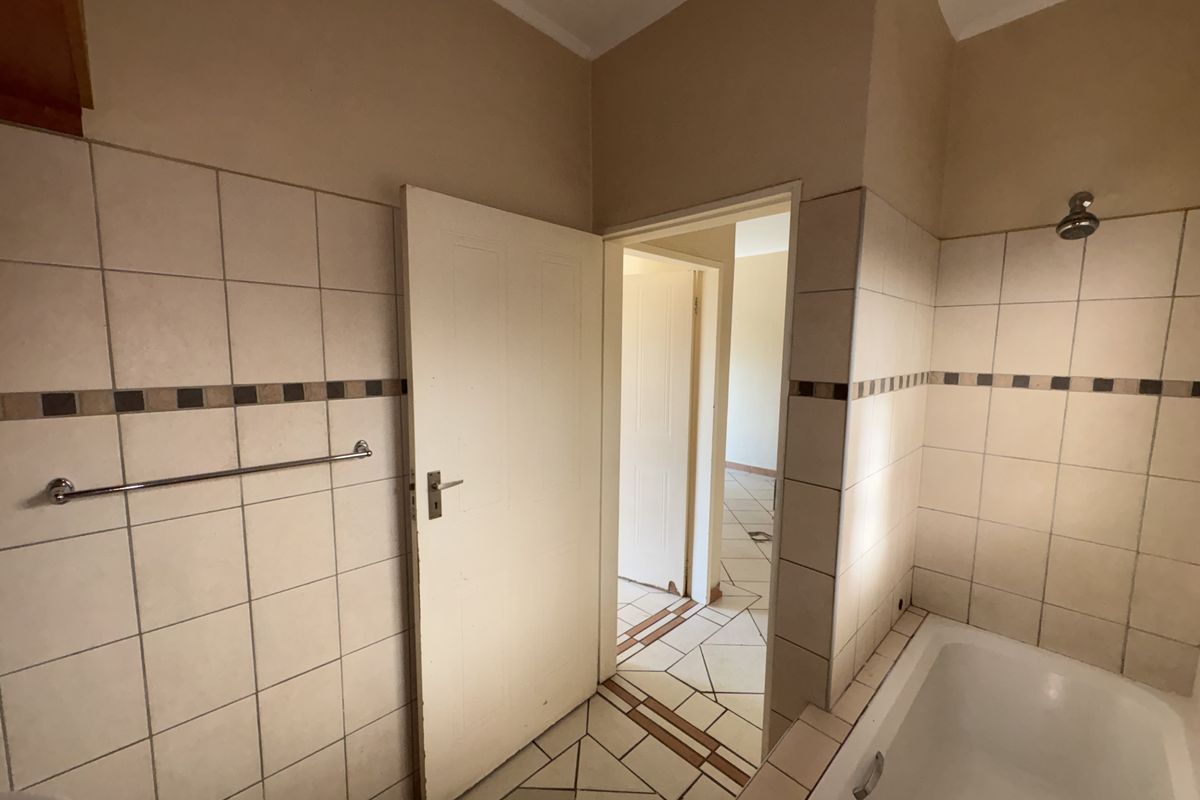 A dated bathroom featuring a bathtub, shower head, and tiled finishes, currently vacant and ready for renovation.