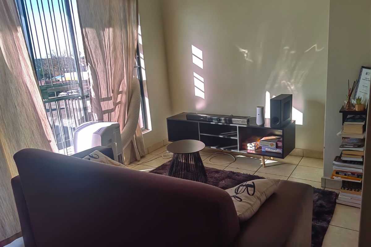 A living room area featuring tiled flooring and a sliding glass door with a security gate, providing access to an outdoor space.