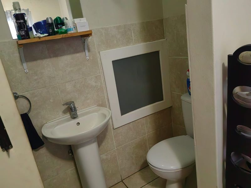 A compact bathroom featuring a pedestal basin, toilet, and neutral wall tiling with a small frosted window for privacy.