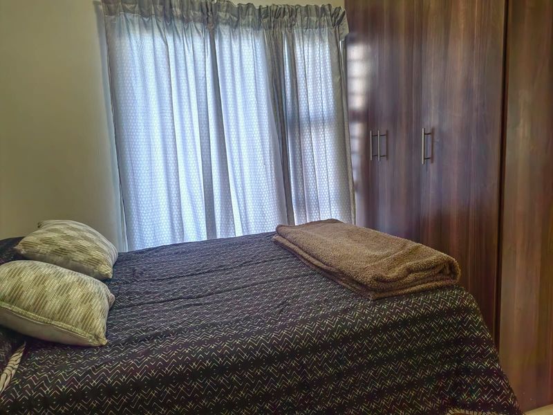 A bedroom featuring built-in wooden cupboards and natural light filtering through window curtains.