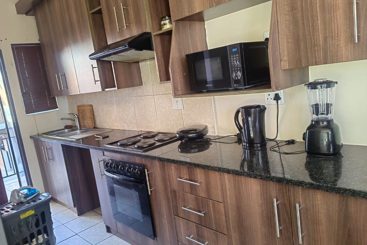 A functional kitchen featuring wood-look laminate cabinetry, granite countertops, a built-in oven with hob, and an extractor fan, with tiled flooring throughout.