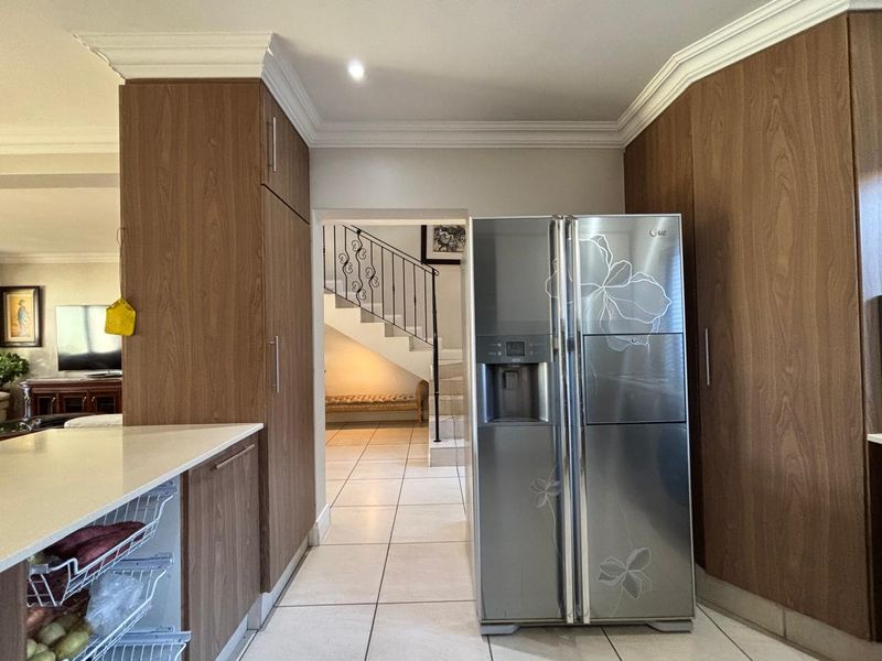 A well-maintained kitchen area featuring wood-finish built-in cabinetry, stone countertops, and tiled flooring, with a clear view through to the staircase.