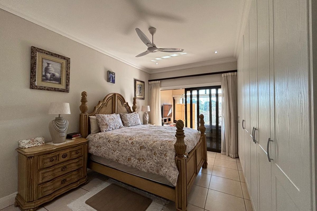 Spacious bedroom featuring neutral tiled flooring, extensive built-in cupboards, a ceiling fan, and sliding glass doors providing access to an outdoor patio area.