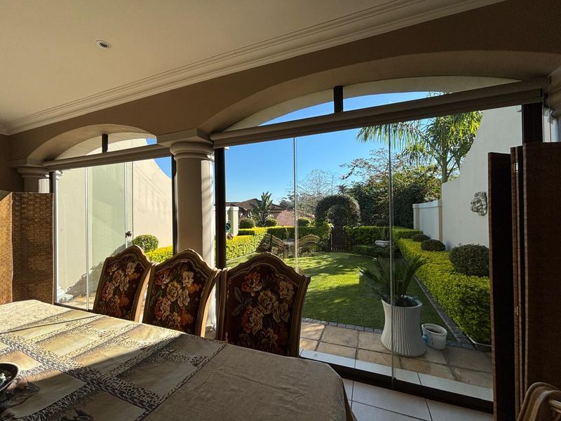 Enclosed patio featuring frameless glass stacking doors, tiled flooring, and recessed lighting, offering a seamless transition to the landscaped garden.