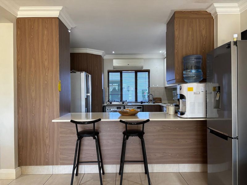 A functional kitchen featuring wood-finish cabinetry, stone countertops, a breakfast bar, and tiled flooring, providing a practical and well-organized culinary space.