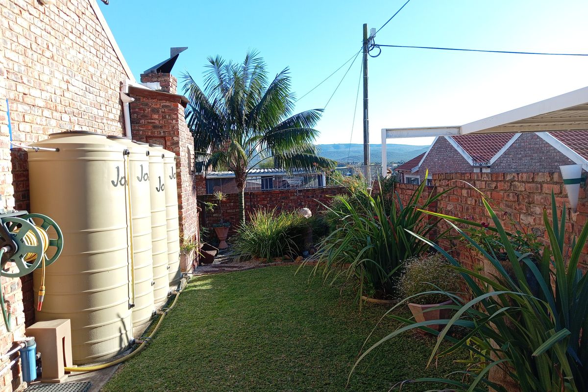 A rear garden area featuring a lawn, established landscaping, and a row of water storage tanks against a brick wall.