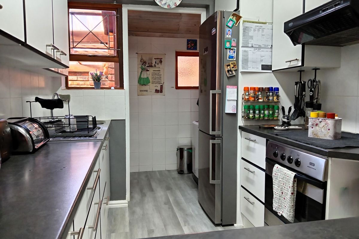 A functional kitchen featuring white cabinetry, dark laminate countertops, a built-in oven with extractor fan, and a tiled splashback, leading into a utility area.