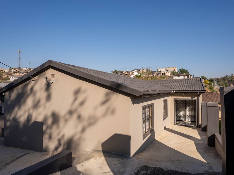 Rear view of a modern house featuring a tiled roof, concrete paved area, and secure entrance gate.