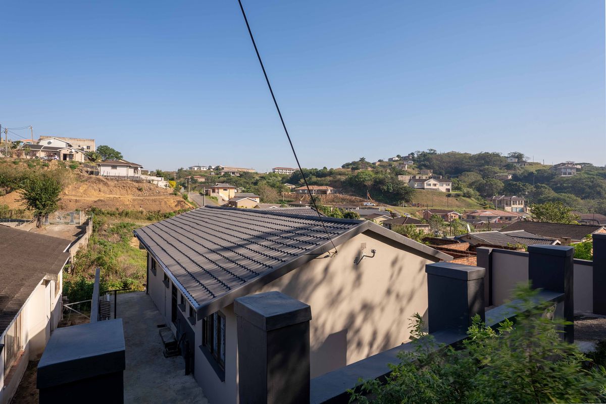 Elevated rear view of the property showing the tiled roof, concrete boundary walls, and surrounding residential neighborhood landscape.
