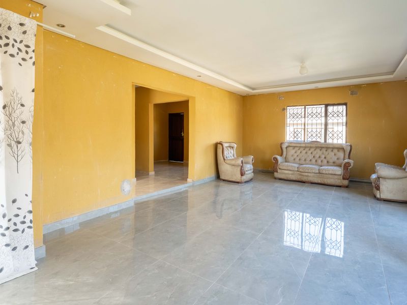 Spacious living room featuring tiled flooring, recessed ceiling details, and security-fitted windows, requiring cosmetic updates to the wall finishes.