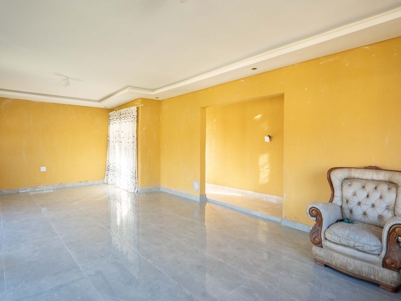 Spacious living area featuring neutral tiled flooring, recessed ceiling details, and yellow painted walls requiring cosmetic attention.