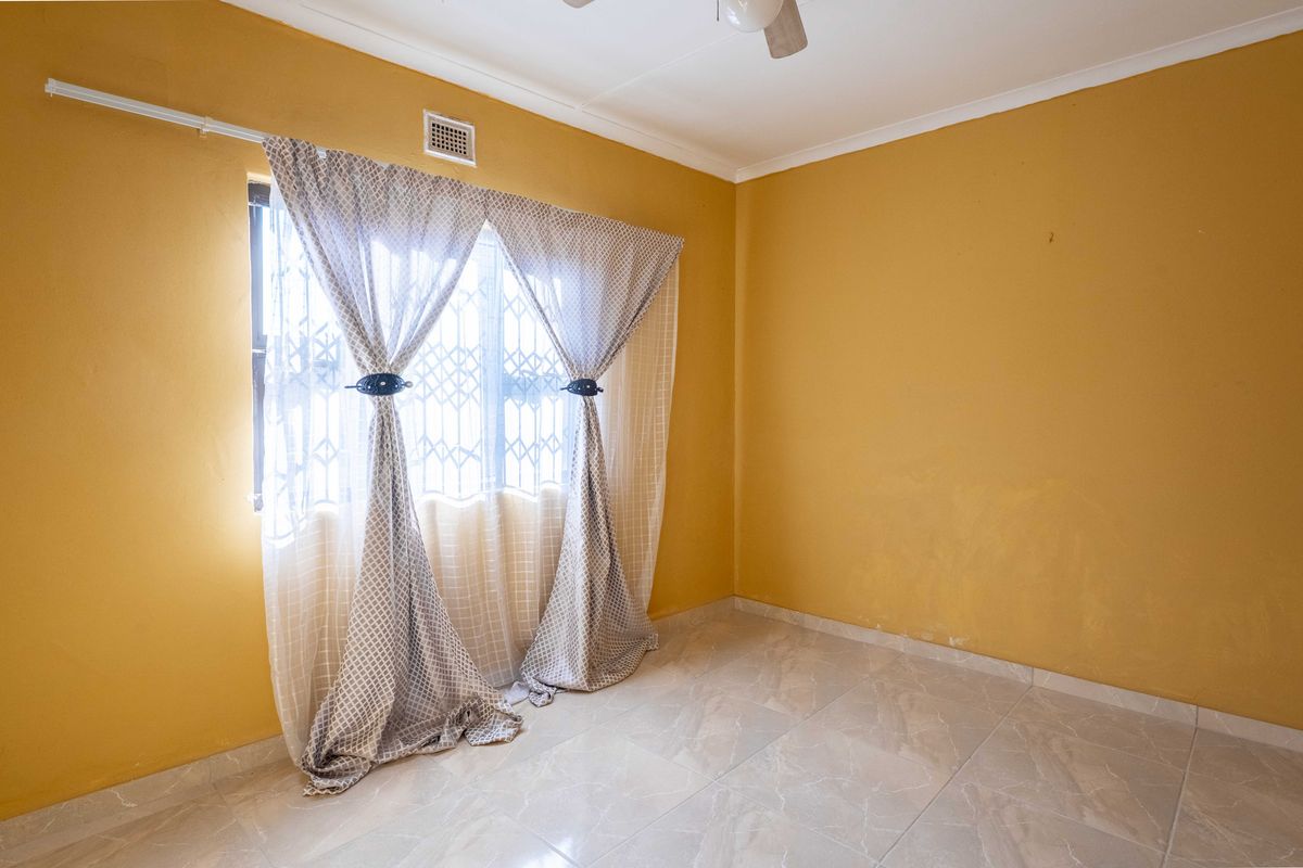 A vacant bedroom featuring tiled flooring, a ceiling fan, and a window fitted with a security gate.