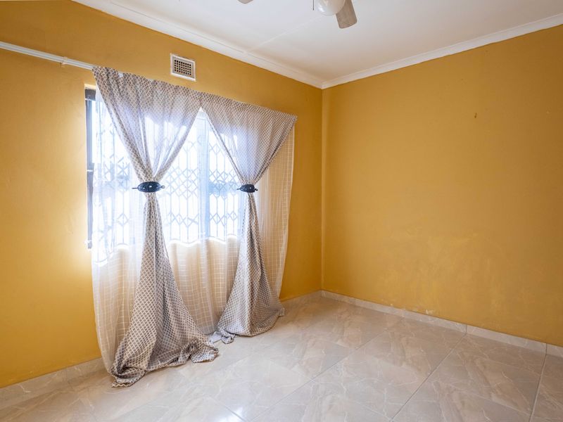 A vacant bedroom featuring tiled flooring, a ceiling fan, and a window fitted with a security gate.