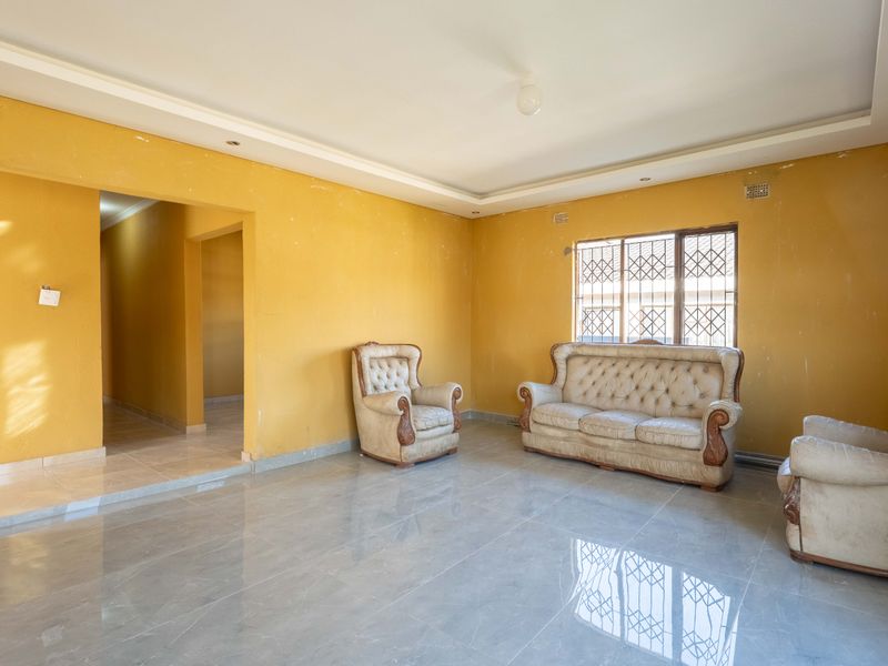 Spacious living room featuring large format floor tiles, recessed ceiling detail, and security bars on the window.