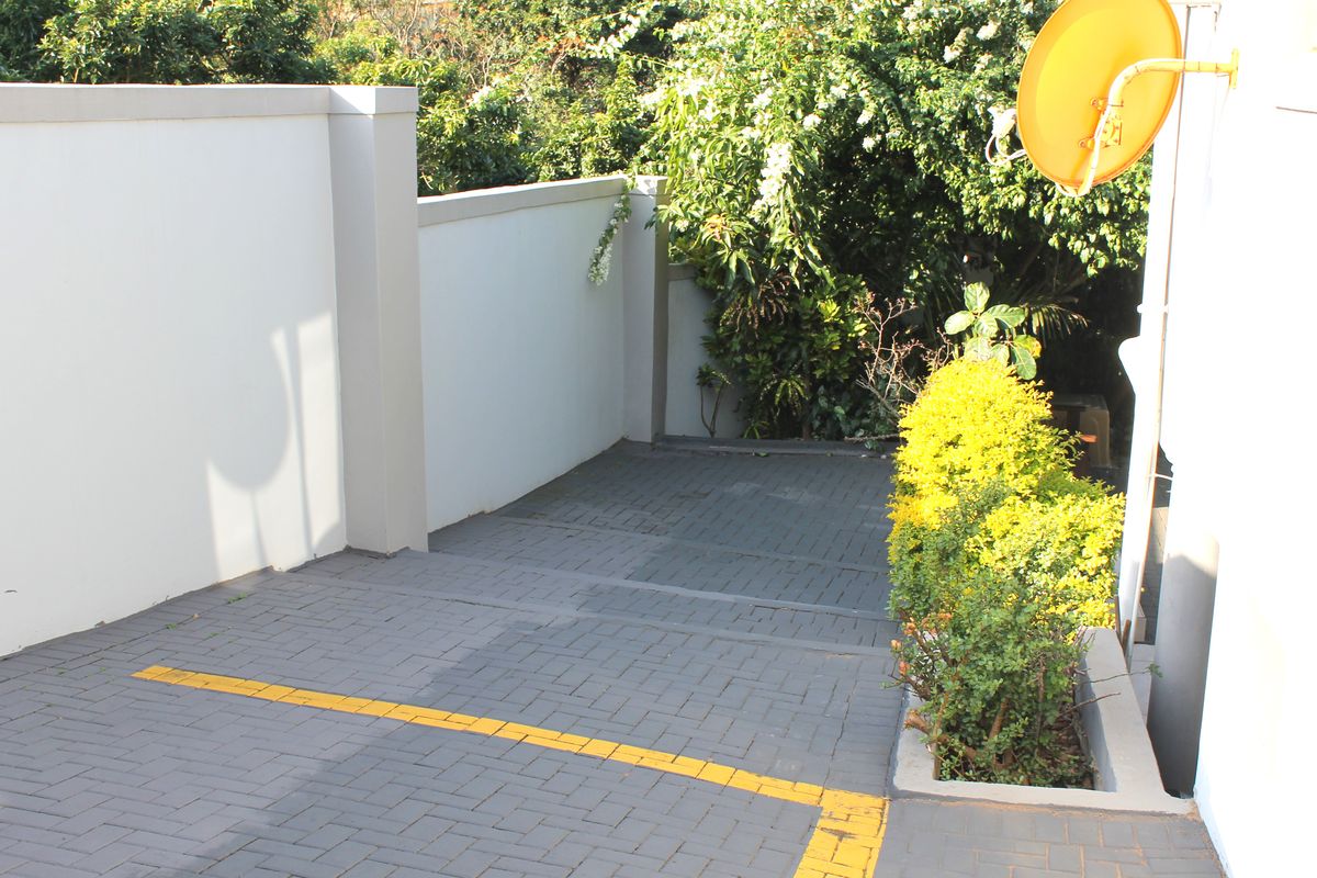 A paved rear driveway area featuring a boundary wall and a mounted satellite dish, surrounded by established garden greenery.