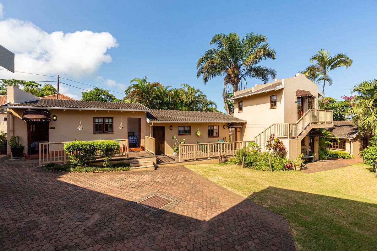 A well-maintained guest house exterior featuring a brick-paved courtyard, timber decking, and an external staircase leading to an upper level.