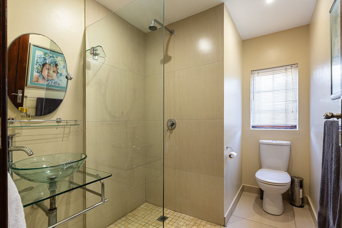A modern bathroom featuring a glass vessel sink, a walk-in shower with a frameless glass screen, and neutral floor-to-ceiling tiling.