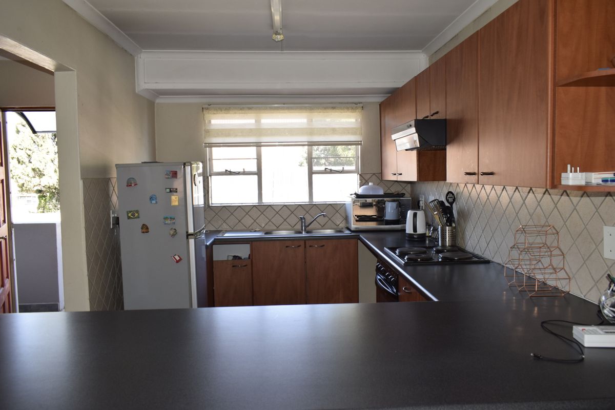 A functional kitchen featuring wooden cabinetry, laminate countertops, a built-in hob with extractor fan, and a tiled backsplash with a window for natural light.